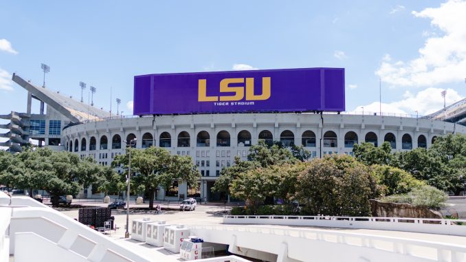 Exterior view of LSU's Tiger Stadium with a large purple LSU sign on top against a blue sky.