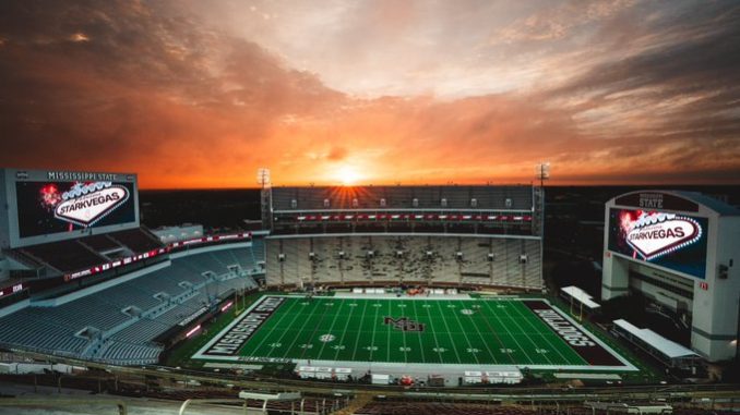 Mississippi State football stadium at sunset, empty stands with a green field and illuminated video boards reading 'Mississippi State Starkvegas'.