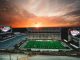 Mississippi State football stadium at sunset, empty stands with a green field and illuminated video boards reading 'Mississippi State Starkvegas'.