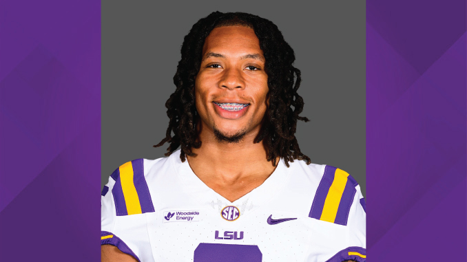 Portrait of an LSU football player in a white jersey with purple and gold stripes, smiling with braces against a gray backdrop.