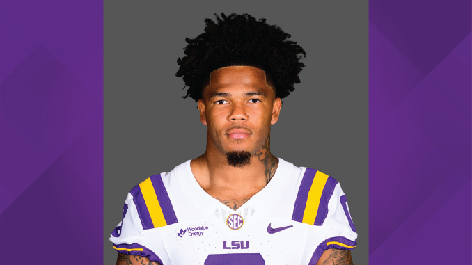 Portrait of an LSU football player in a white jersey with purple and gold stripes, facing the camera against a gray backdrop.