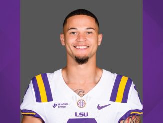 Portrait of an LSU football player in a white jersey with purple and gold stripes, smiling at the camera.