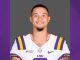Portrait of an LSU football player in a white jersey with purple and gold stripes, smiling at the camera.