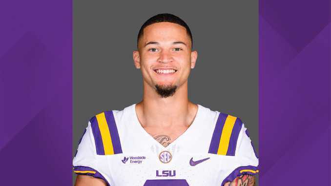 Portrait of an LSU football player in a white jersey with purple and gold stripes, smiling at the camera.