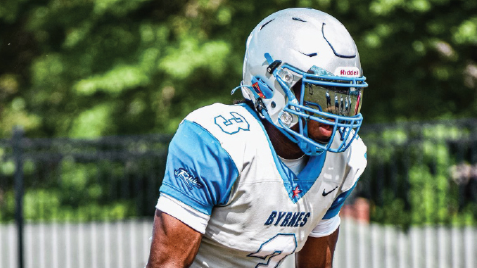 Football player in BYNES white and light blue uniform crouches on the field, wearing a blue helmet with a facemask.