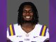 Portrait of an LSU football player smiling, wearing a white jersey with purple and gold stripes and LSU logo.