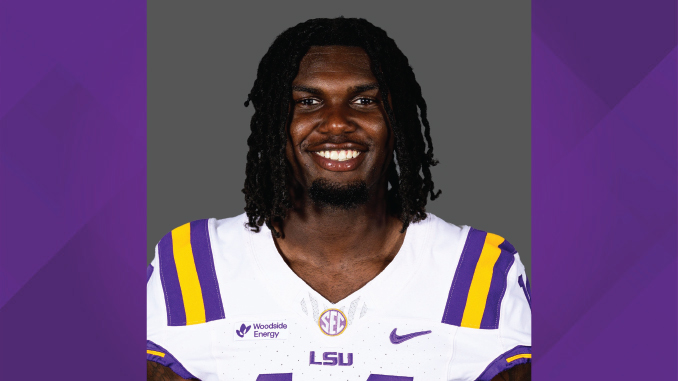 Portrait of an LSU football player smiling, wearing a white jersey with purple and gold stripes and LSU logo.