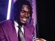 Smiling man in a purple suit and patterned tie, holding a basketball at an indoor event with purple lighting behind him