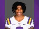 Portrait of a college football player in an LSU jersey, smiling at the camera against a gray backdrop.