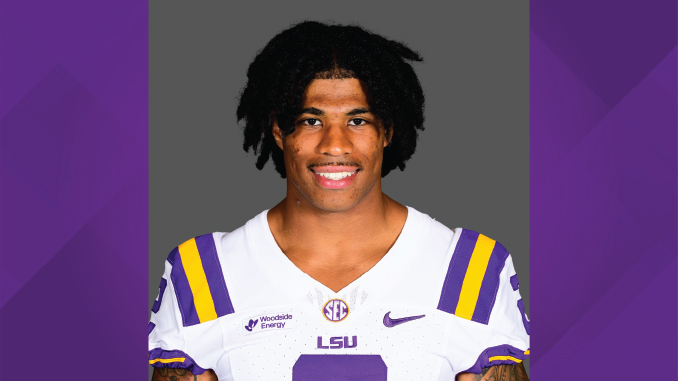 Portrait of a college football player in an LSU jersey, smiling at the camera against a gray backdrop.