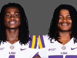 Two LSU football players with long dreadlocks stand side by side in white jerseys with purple and gold accents against a gray backdrop, smiling slightly.