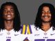 Two LSU football players with long dreadlocks stand side by side in white jerseys with purple and gold accents against a gray backdrop, smiling slightly.