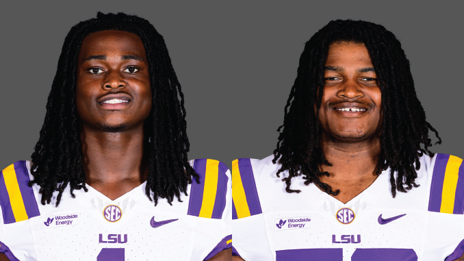 Two LSU football players with long dreadlocks stand side by side in white jerseys with purple and gold accents against a gray backdrop, smiling slightly.
