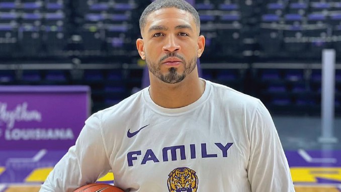 Basketball player in a gym holding a basketball, wearing a gray shirt that says 'FAMILY' with a tiger logo beneath it.
