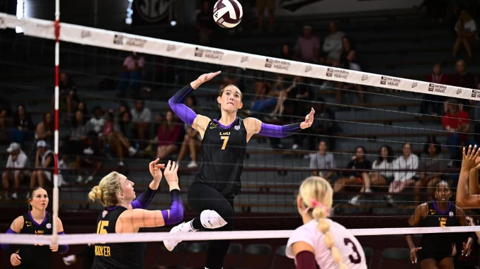 LSU volleyball player leaps to spike the ball over the net as teammates watch nearby.