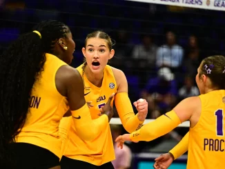Louisiana State University women's volleyball players celebrate on the court in yellow uniforms, central player with mouth open in a cheer.