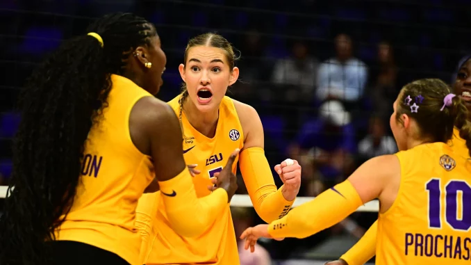 Louisiana State University women's volleyball players celebrate on the court in yellow uniforms, central player with mouth open in a cheer.