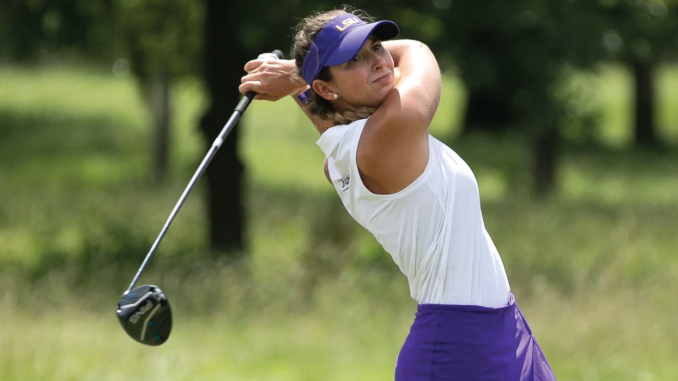 Female golfer in a white sleeveless top and purple visor swinging a driver on a green golf course as trees blur in the background.