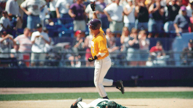 Baseball player in a yellow uniform runs past a fallen catcher on the infield as fans watch from the stands.