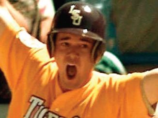 Baseball player in an orange jersey and helmet, arms raised in celebration with an open-mouthed shout.