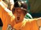 Baseball player in an orange jersey and helmet, arms raised in celebration with an open-mouthed shout.