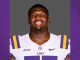 Portrait of an LSU football player smiling, wearing a white jersey with purple and gold stripes and LSU branding.
