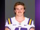 Portrait of a man in an LSU football uniform (white jersey with purple and gold stripes) against a gray background.