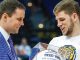 Coach in a blue checkered suit hands a glass trophy to a LSU athlete in a white shirt, both smiling.