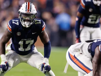 Auburn Tigers football player in navy jersey (number 13) and white pants lunges forward on the field during a game, helmet with orange stripe.