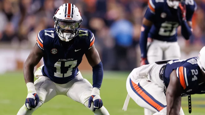 Auburn Tigers football player in navy jersey (number 13) and white pants lunges forward on the field during a game, helmet with orange stripe.