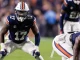 Auburn Tigers football player in navy jersey (number 13) and white pants lunges forward on the field during a game, helmet with orange stripe.