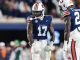 Two Auburn Tigers football players in blue jerseys on the field, #13 facing forward and #24 to the right, with fans blurred in the background.
